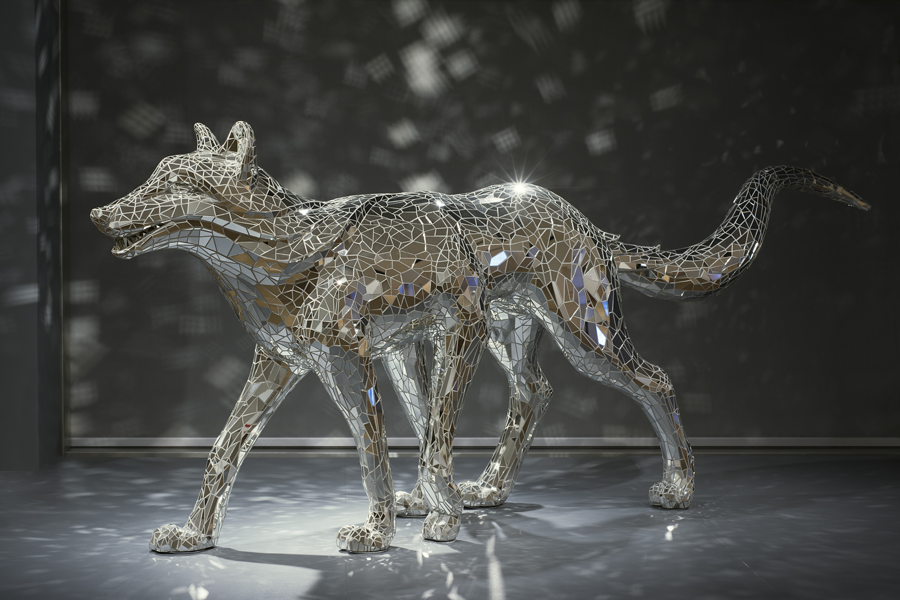 A six-legged wolf covered in a mosaic of sparkling mirrors walks with its tail raised and mouth slightly open