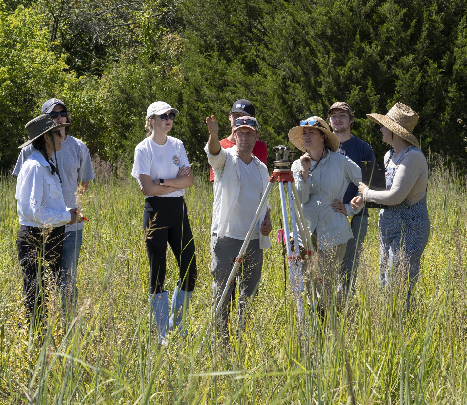 A group of people standing in a field around an instrument on a tripod