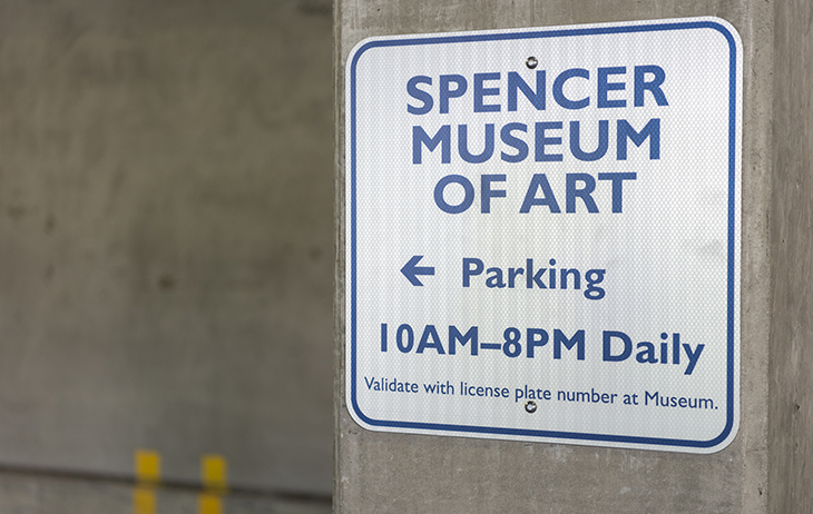 A white sign with blue text reads "Spencer Museum of Art Parking"