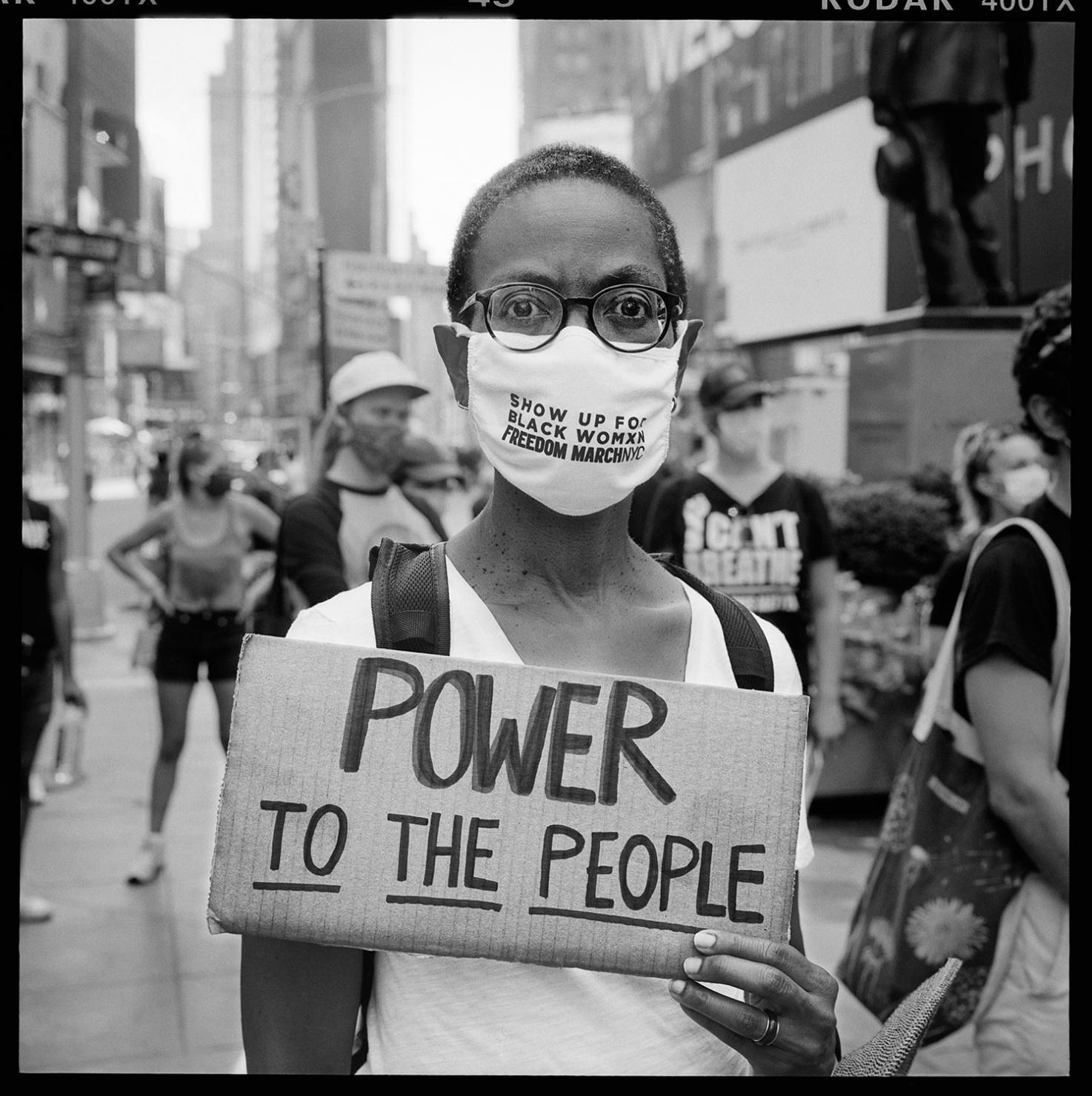 A person in glasses holding a cardboard sign that reads "Power to the people"