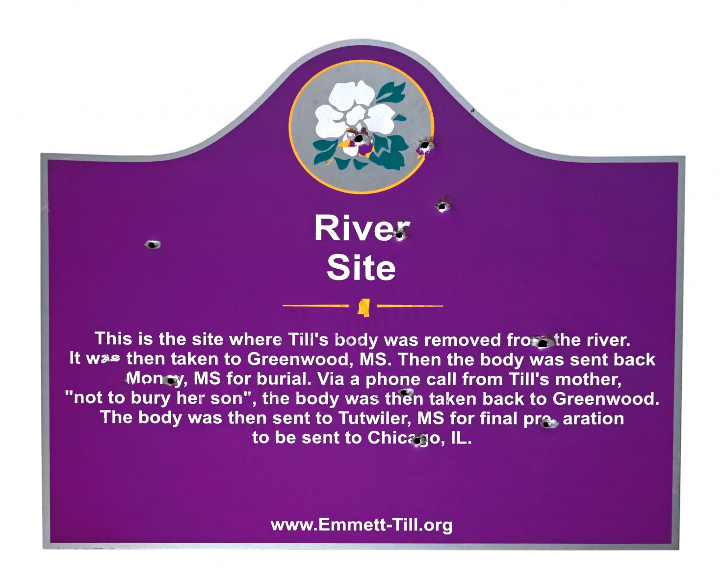 purple sign with bullet holes and a paragraph of white text that begins "River Site: This is the site where Emmett Till's body was removed from the river."