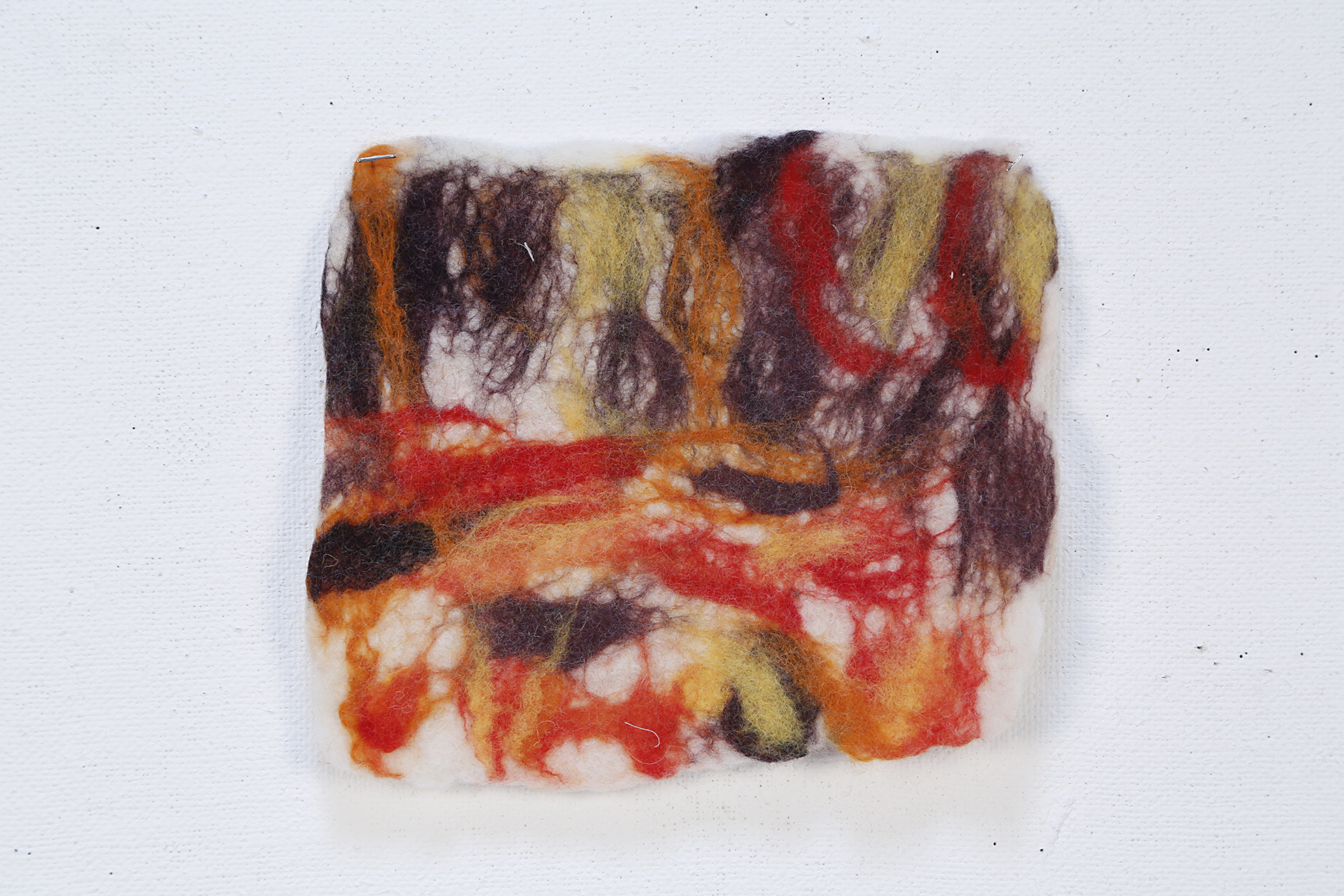 Dark purple, orange, yellow and red fibers blend together as wisps against a white background
