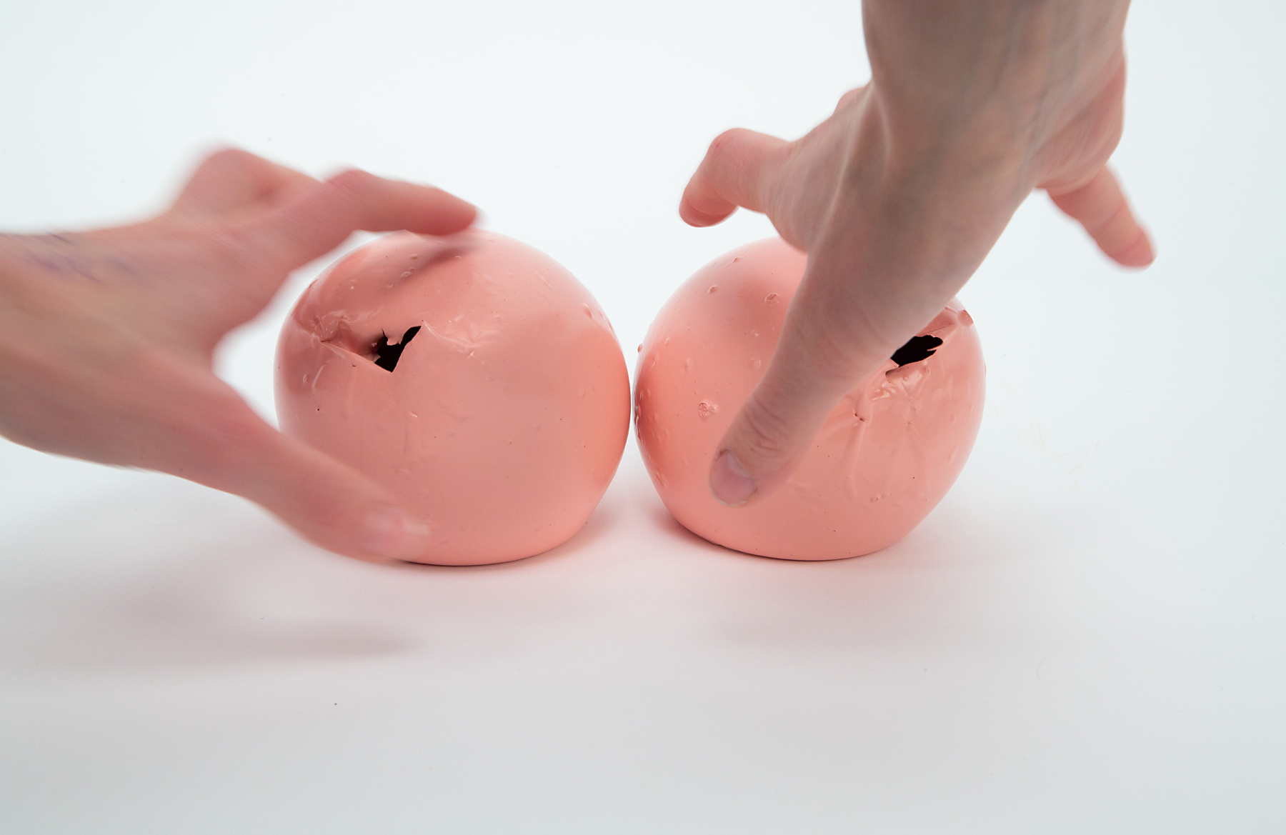 To hands reach toward two pink spheres as if they are about to squeeze them. 