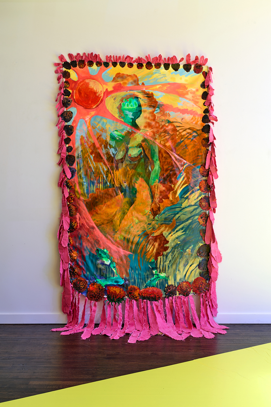 Mixed-media artwork featuring a green humanlike figure among a colorful landscape under a bright red sun surrounded by bright pink fabric fringe  