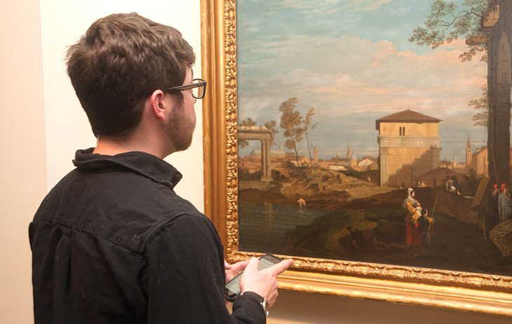 Man in front of painting holding a mobile phone