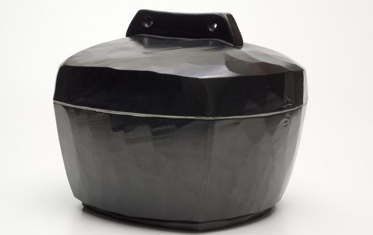 a shiny, black, slightly oblong pot with a shallow lid that has a slim rectangular handle with small holes at each end
