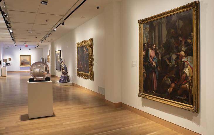 A gallery with a long wall on the right with large paintings and in the center a clear, circular sculpture