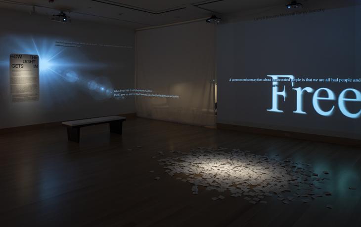 A dark room with white text projected on the wall and a pile of paper in the center of the room