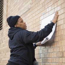 Bell begins to unroll and affix her artwork <i>Charlottesville</i> to the west wall of Chalmers Hall. This large-scale installation is part of Bell's <i>Counternarratives</i> series that questions and revises racial bias in media. 