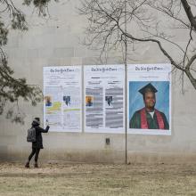 A student takes a picture of Bell's <i>A Teenager with Promise, Annotated</i> installation on the side of Watson Library. This artwork is part of Bell's <i>Counternarratives</i> series.  