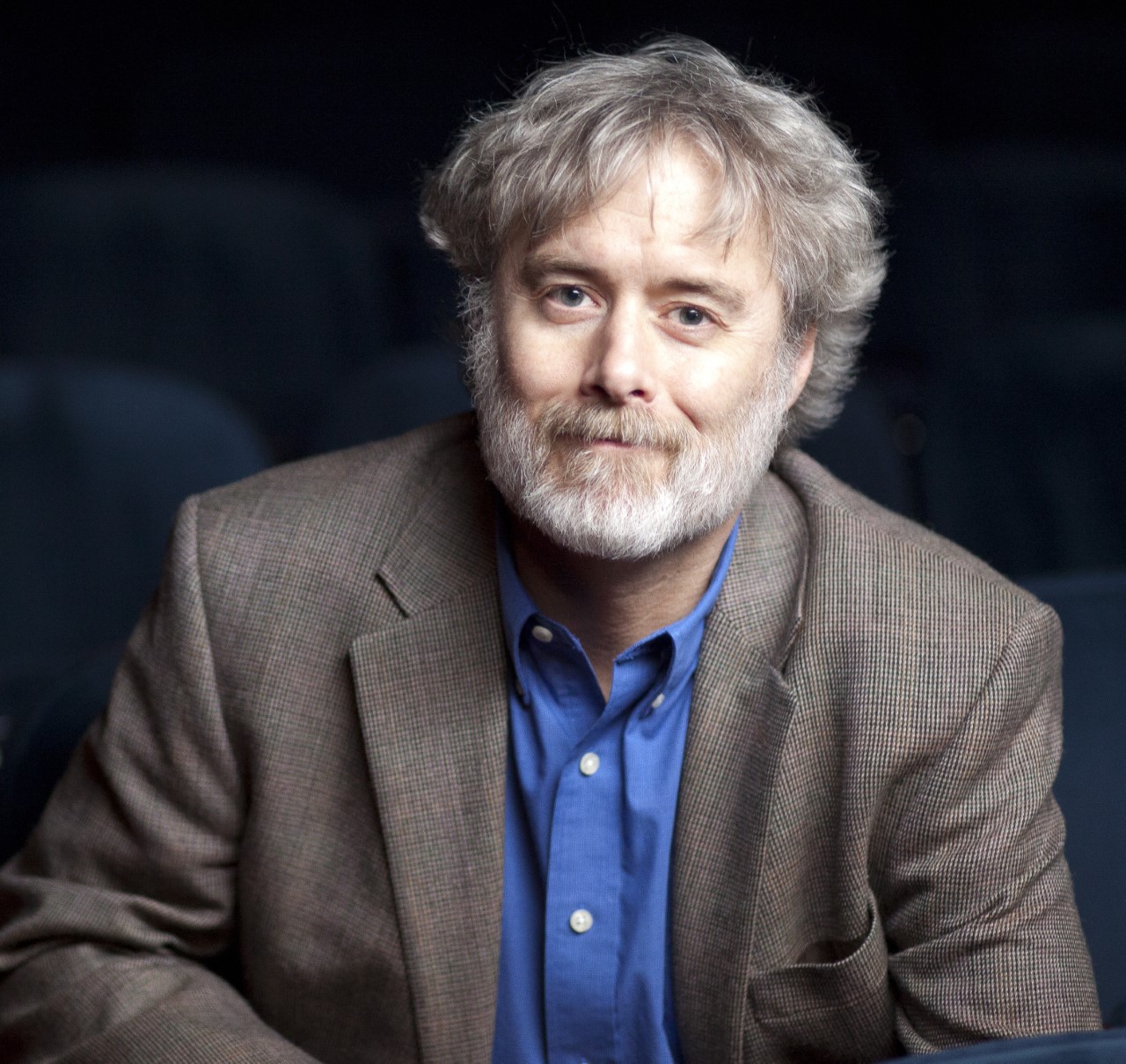 Color photograph of a man (Perry Alexander) with gray hair and a beard wearing a blue shirt and light brown suit jacket